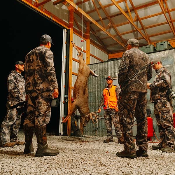 Hunters standing around a deer talking about their hunts